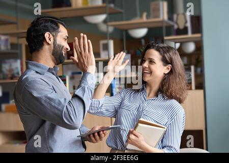 Two happy friendly diverse professionals giving high five standing in office. Stock Photo