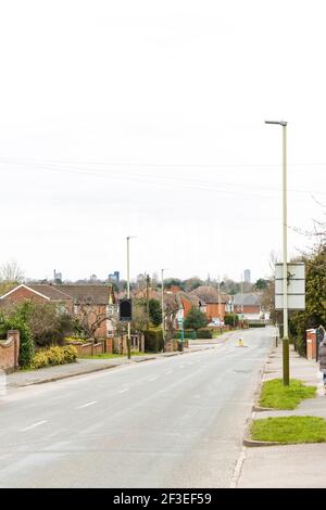 Long suburban road with small pedestrian crossing. Shows houses and pavement either side, with Leicester city skyline in the background. Stock Photo