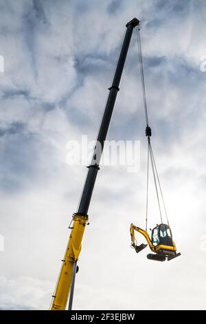 Hydraulic crane telescopic boom detail moving track excavator on cloudy sky background. Yellow jib of mobile vehicle hoist device carrying earthmover. Stock Photo