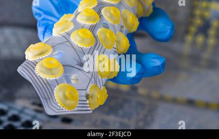 Silicone flex printed circuit board curled to a roll on computer keyboard membranes background. Engineer hand with plastic flexible PCB. Yellow button. Stock Photo