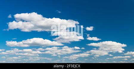 Group of idyllic floating white clouds on azure blue sky background. Tranquil natural panoramic cloudscape scene. Environment, weather or meteorology. Stock Photo