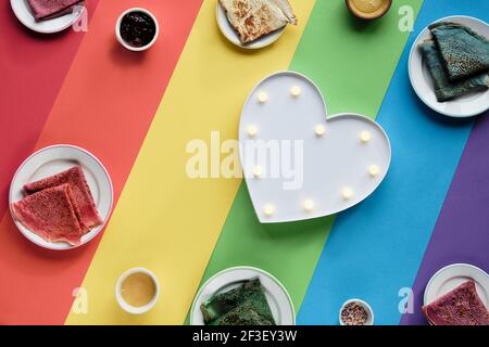 Rainbow pancakes, different color crepes. Spinach, beetroot powder, blue matcha and turmeric crepes. Colorful pancakes, flat lay on rainbow layered Stock Photo