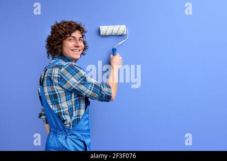 Man in working clothes repairing wall, using painting tool. Paint work. Paint shop. Renovation and repair. Renewal and redecorating. isolated blue bac Stock Photo