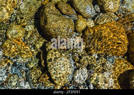 Beautiful Stones and rocks under clear water of a river taken in Ticino, Switzerland.Water background.Summer background.Shallow water.Sunlight glare. Stock Photo