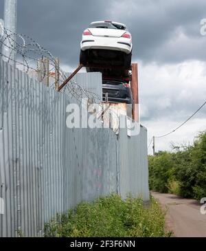 Scrap cars stored high up behind a fence Stock Photo