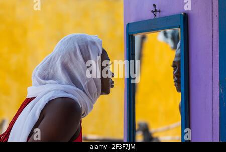 African Ghana woman standing in front of a mirror with a white shawl covering her hair Stock Photo