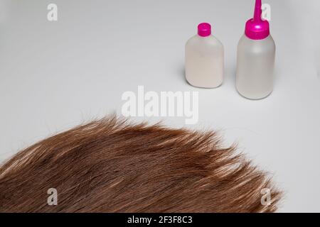 The tips of a woman's long hair lie against a white background. Tubes and jars stand on a white surface. Hair care. Dark brown hair. Stock Photo