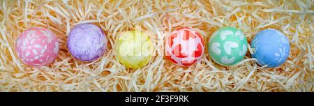 Overhead view of decorated Easter eggs lined up in a row over a background of paper shavings. Eggs painted by a child. Banner Stock Photo