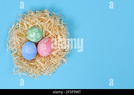 Colorful handmade painted Easter eggs in the nest isolated on a blue background. Easter eggs painted by a child. Top view, copy space Stock Photo