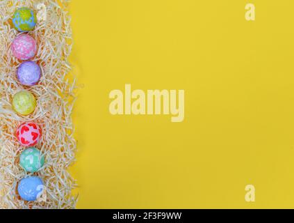 Colorful Easter eggs on paper shavings egg side border against yellow background. Eggs painted by a child. Flat lay style, copy space Stock Photo