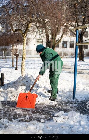 The landlord scrapes snow and ice with an orange cobblestone shovel Stock Photo
