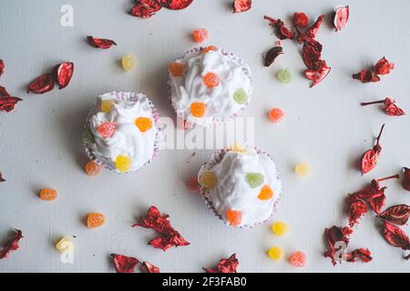 Three cupcakes with jelly beans on white background. Pieces of dry roses around them. Selective focus on different areas. Stock Photo