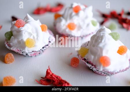 Three cupcakes with jelly beans on white background. Pieces of dry roses around them. Selective focus on different areas. Stock Photo
