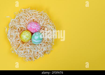 Colorful handmade painted by a child Easter eggs in the nest isolated on a yellow background. Traditional handcraft for Happy Easter. Top view, copy s Stock Photo