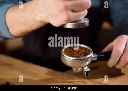 Barista presses ground coffee using tamper in a coffe shop Stock Photo