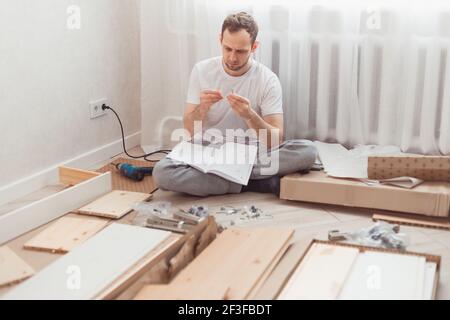 Man self-assemblies wooden furniture at home without master. Read instructions. Diy concept Stock Photo