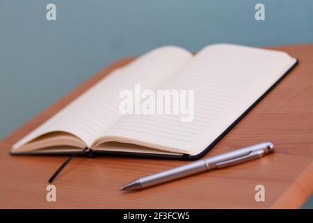 A closeup shot of an opened blank notebook next to a pen Stock Photo
