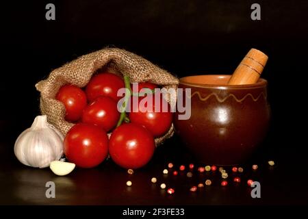 Fresh organic vegetables on a black background. Tomatoes in bagging, clay pot, garlic and spice Stock Photo