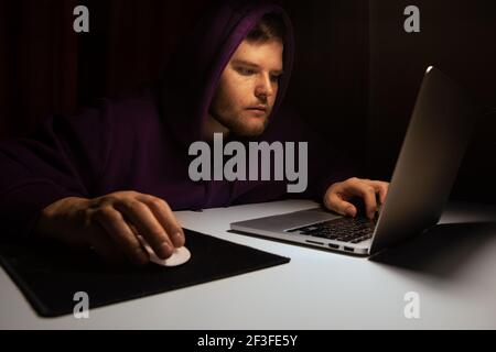 man in hoddie working on laptop till night dark background lamp light Stock Photo
