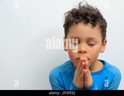 boy praying to God with hands held together with closed eyes on white background stock photo Stock Photo
