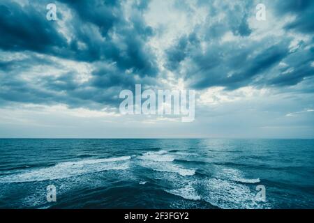 Dark blue clouds and sea or ocean water surface with foam waves before storm, dramatic seascape. Stock Photo