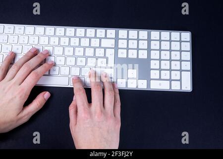 Female hands on the white keyboard on black baground. Typing, writing, freelance and working from home keyboard. Stock Photo