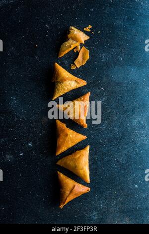 Samosa triangles placed in a pattern on a black tile surface Stock Photo