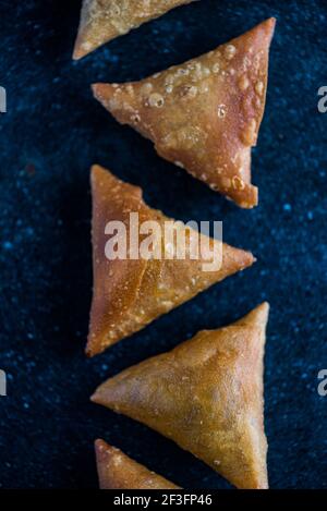 Samosa triangles placed in a pattern on a black surface Stock Photo
