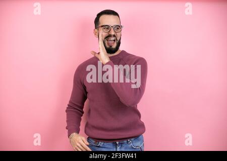 Handsome man wearing glasses and casual clothes over pink background hand on mouth telling secret rumor, whispering malicious talk conversation