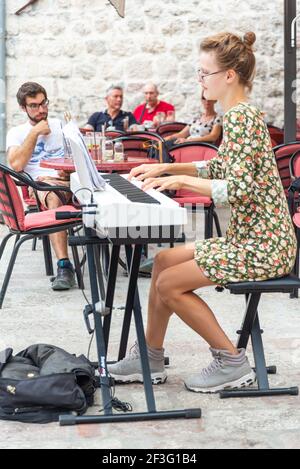 Classical pianist performs for tourists in a main square in Old Town, Kotor,Montenegro.Playing her electric keyboard while surrounded by cafes and res Stock Photo