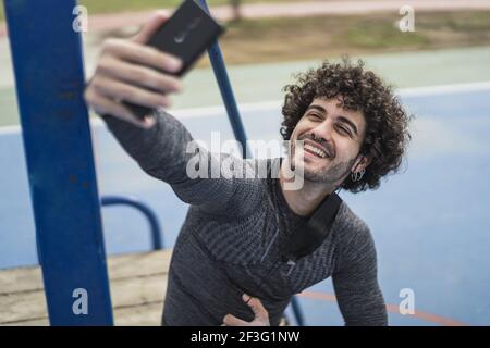 An attractive smiling Spanish male with a mask hanging on the ear and taking a selfie Stock Photo