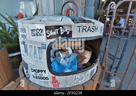 Over full trash can in Berkeley near where so many homeless put garbage, which is covered with stickers about political ideas Stock Photo