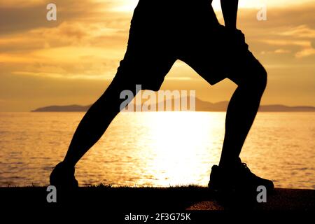 Silhouette of a man lower body, stretching at the beaach in twilight Stock Photo