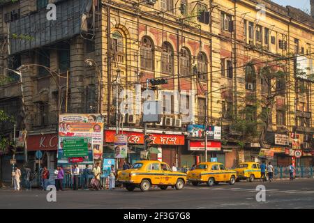 Yellow taxi waiting for passengers at city road crossing with view of old Government office building at Kolkata India Stock Photo