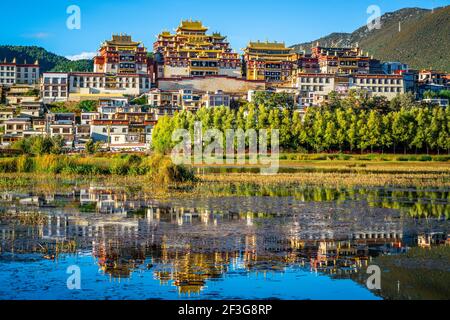 Beautiful scenic view of Ganden Sumtseling monastery with water reflection at sunset and blue sky in Shangri-La Yunnan China Stock Photo