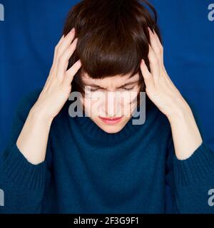 Portrait of mature woman in distress, close-up. Agitated tensed face. Bright dark blue wall Stock Photo