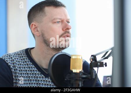 Young man sitting in front of microphone in recording studio Stock Photo