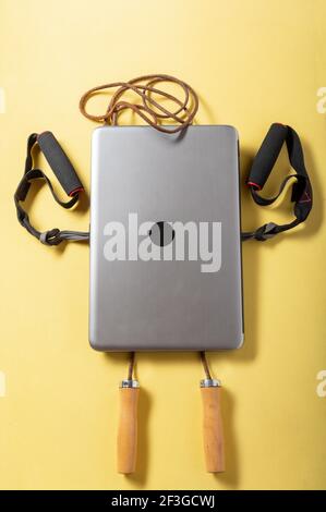 Robot man. Laptop in the shape of a sports man. Fitness simulators and laptop beech on a yellow background. Vertical frame. Stock Photo
