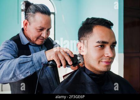 latin man stylist cutting hair to a client in a barber shop in Mexico Stock Photo