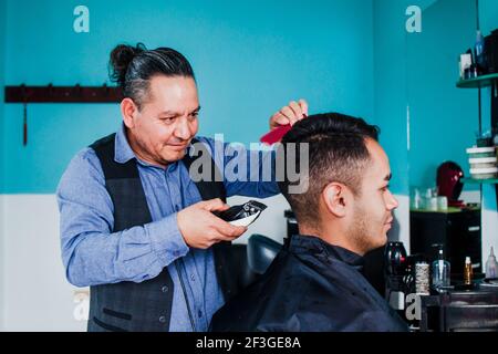 latin man stylist cutting hair to a client in a barber shop in Mexico Stock Photo