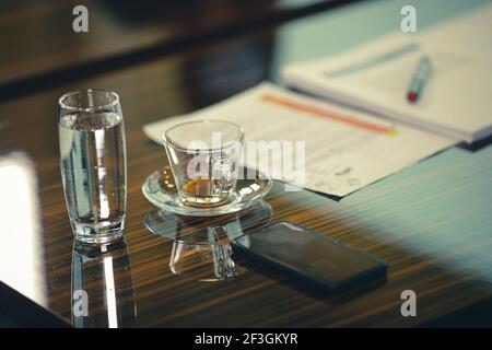 Shallow depth of field (selective focus) image with an empty coffee cup and a glass of sparkling water on the desk of a businessman during a corporate Stock Photo