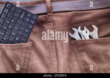 Spanners and computer keyboard in brown jeans pockets, technical support or smart tools concept Stock Photo