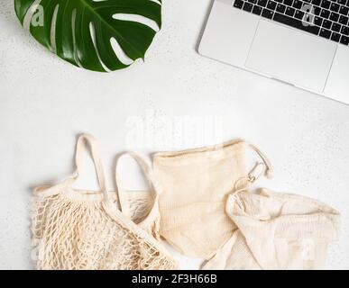 Various bags with drawstring, string bag eco sack made from natural cotton fabric cloth and laptop flat lay on light grey background. Top view. Copy s Stock Photo