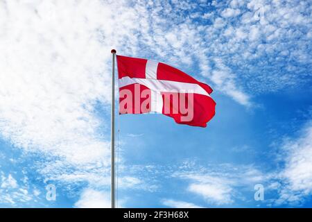 Danish flag on blue sky. Flag of Denmark waving in the wind. Bright and colourful concept for travel and tourism.