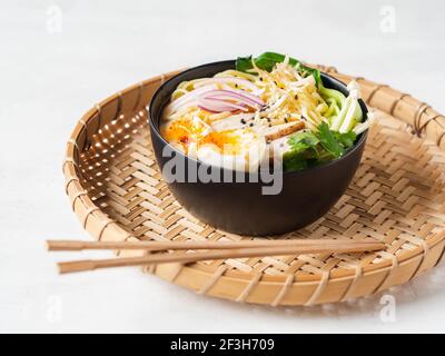 Chicken ramen noodle soup with meat, bok choy, mushrooms, egg in black bowl on grey background. copy space Stock Photo