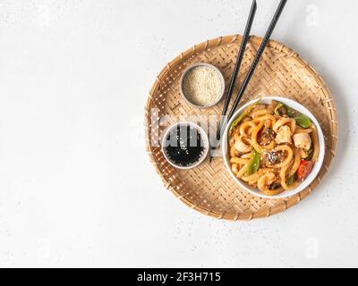 Udon noodles with seafood and vegetables cooked in a wok in a white bowl on a wicker tray. Top view. Copy space Stock Photo