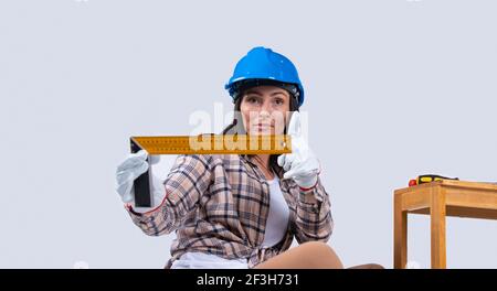 Engineer woman in a blue hard hat and gloves holds a level, a ruler on a white background with side space. Stock Photo