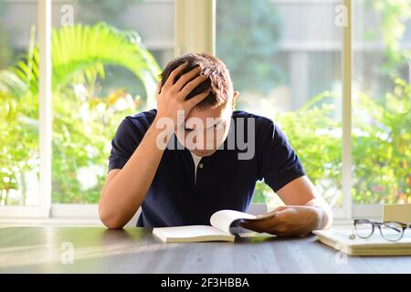 Stressed man reading book with hand on his head - studying & examination concepts Stock Photo