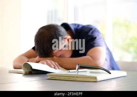 Young man sleeping on the table with book opened, weary & tired of reading (studying) Stock Photo