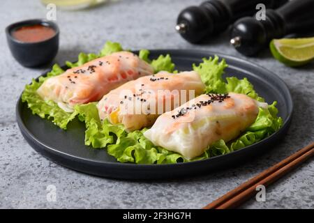 Asian food spring rolls with shrimps, vegetables wrapped in rice paper on grey background. Close up. Vietnamese cuisine. Stock Photo